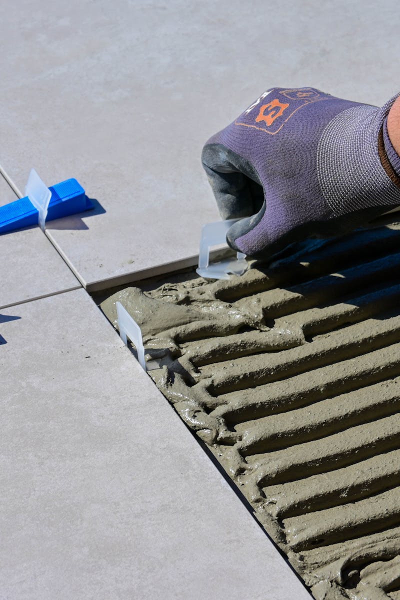Detailed view of gloved hand aligning tiles with levelers and spacers during construction.