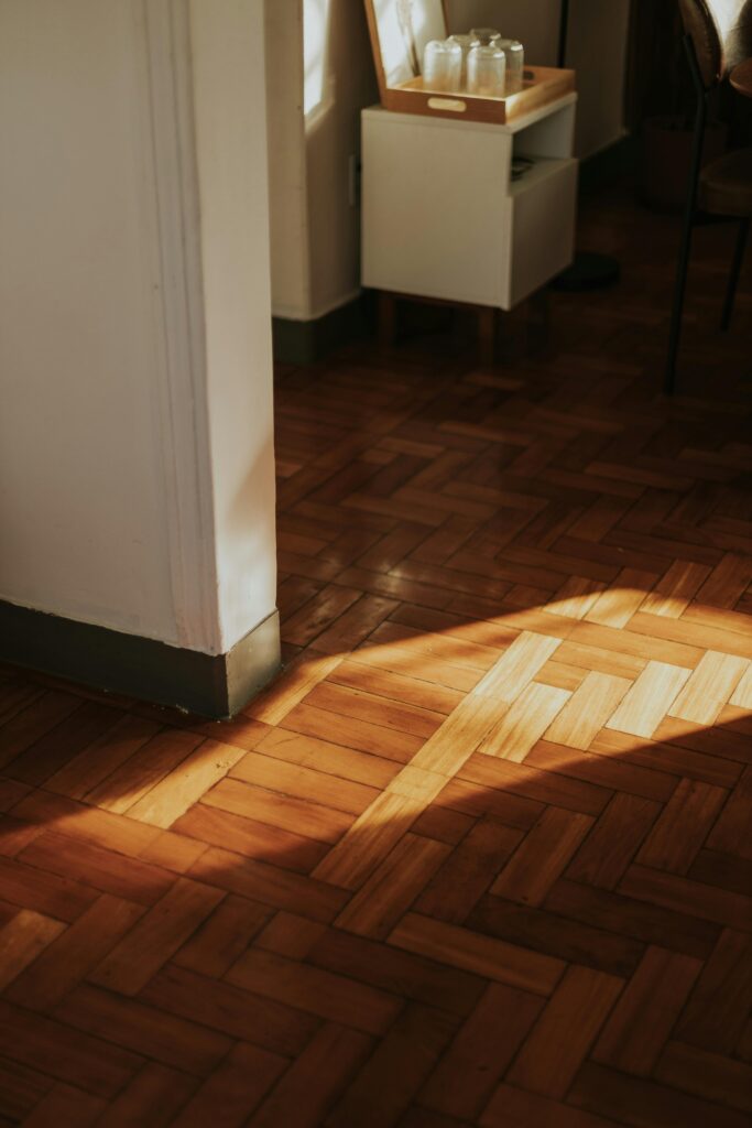 pexels-photo-36178801-36178801 Warm sunlight cast on wooden parquet flooring in a cozy indoor setting.